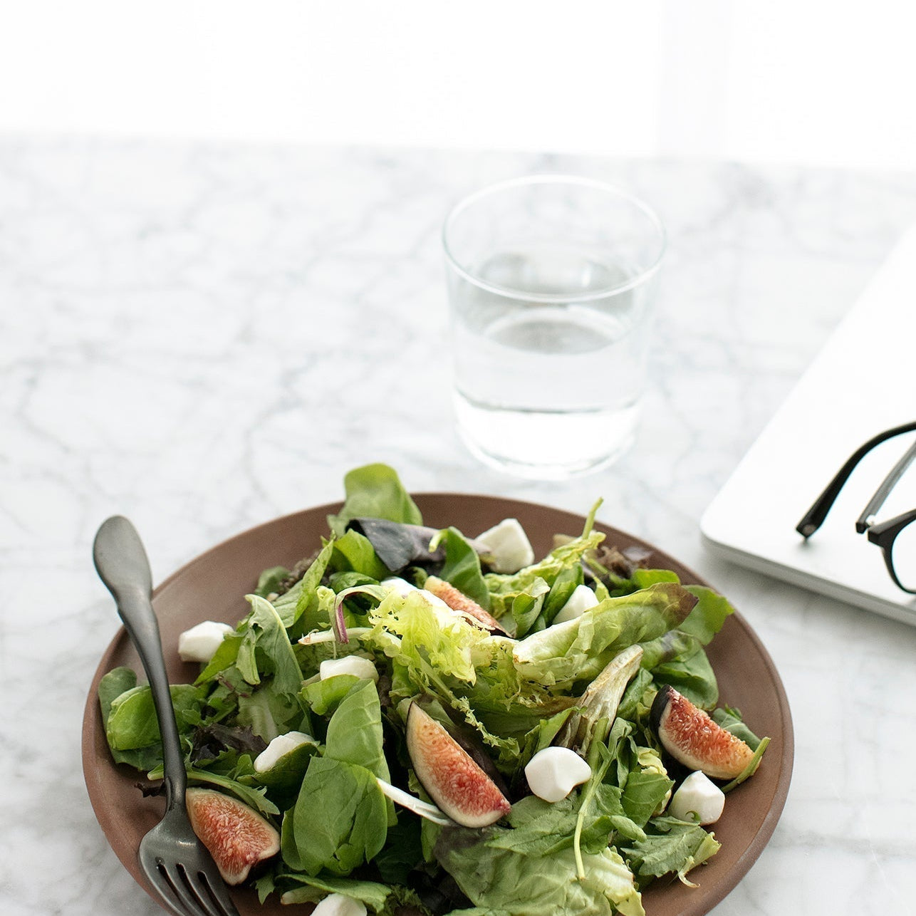 Plate of leafy greens with figs beside a glass of water, representing nutrient-rich food for energy production