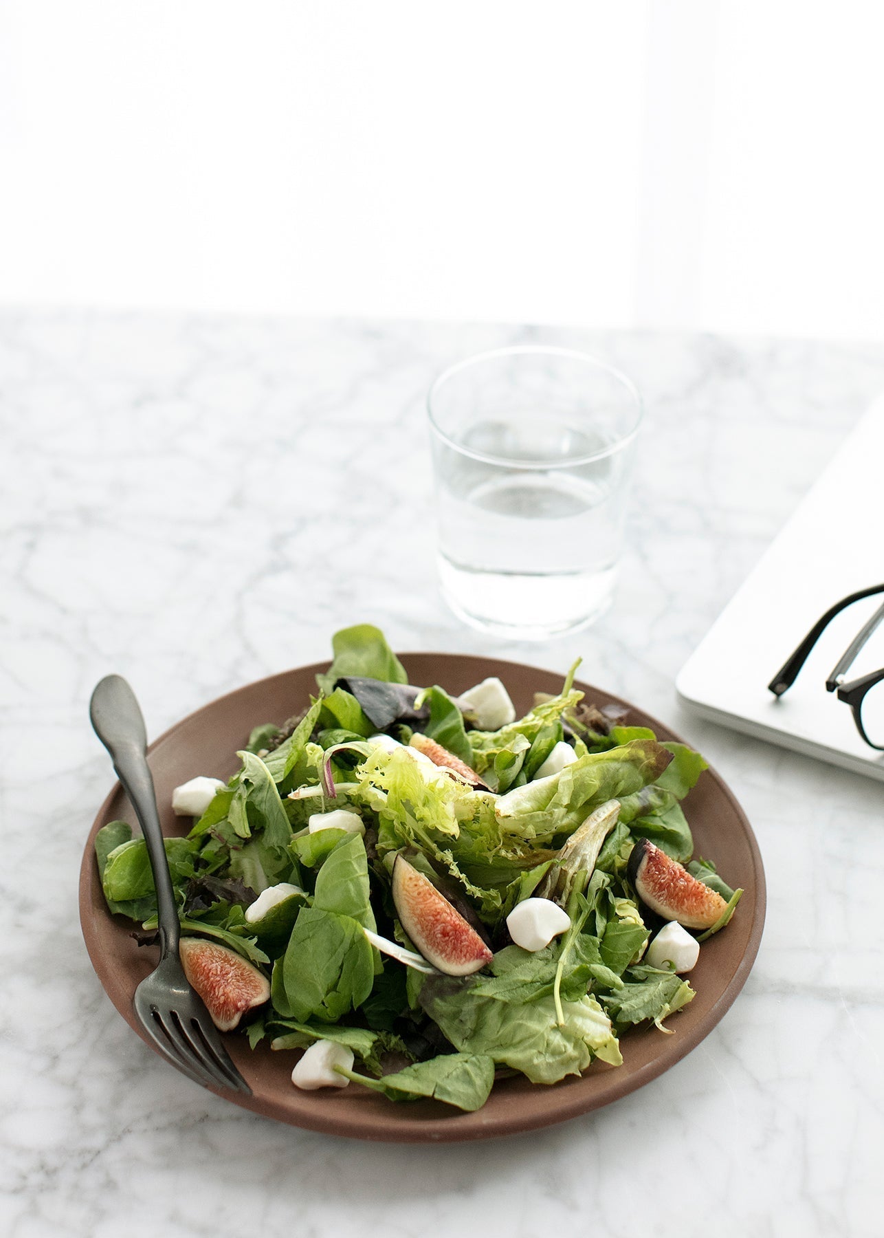 Plate of leafy greens with figs beside a glass of water, representing nutrient-rich food for energy production