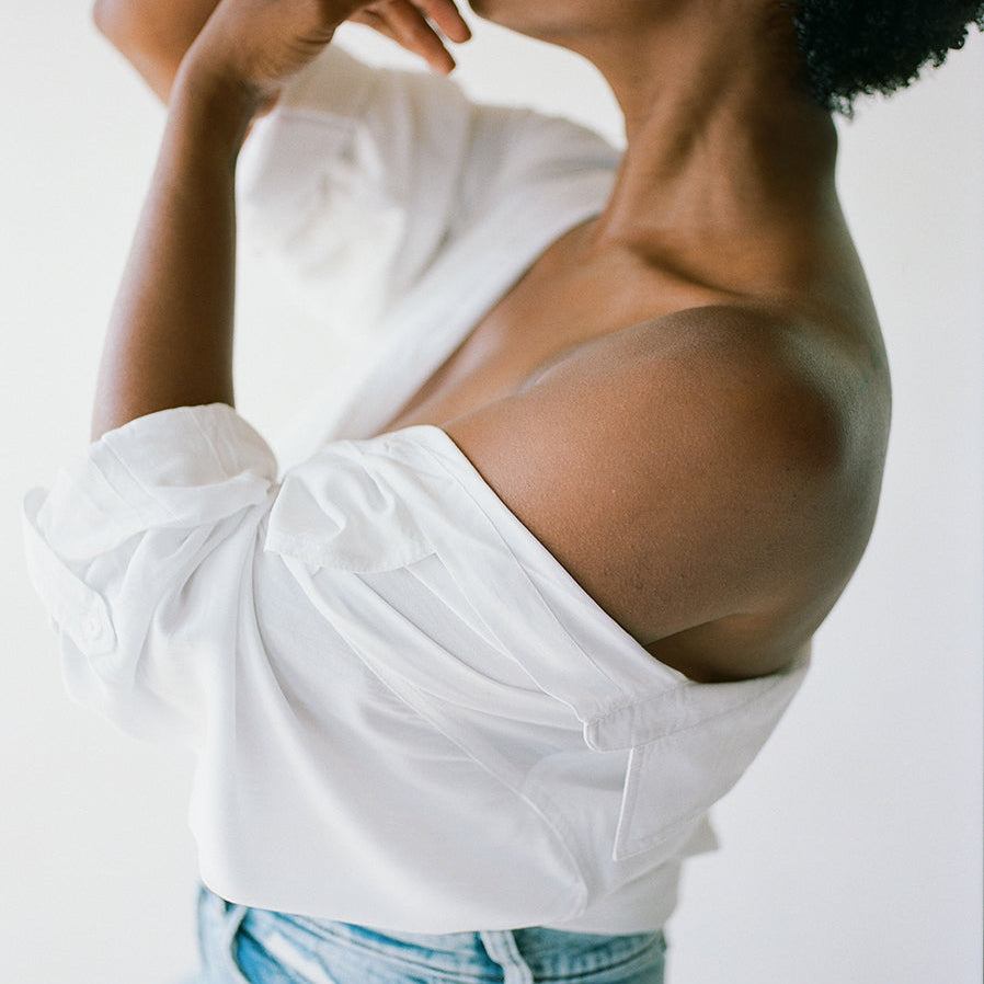 Woman in an off-the-shoulder white shirt in profile, hand near her lips