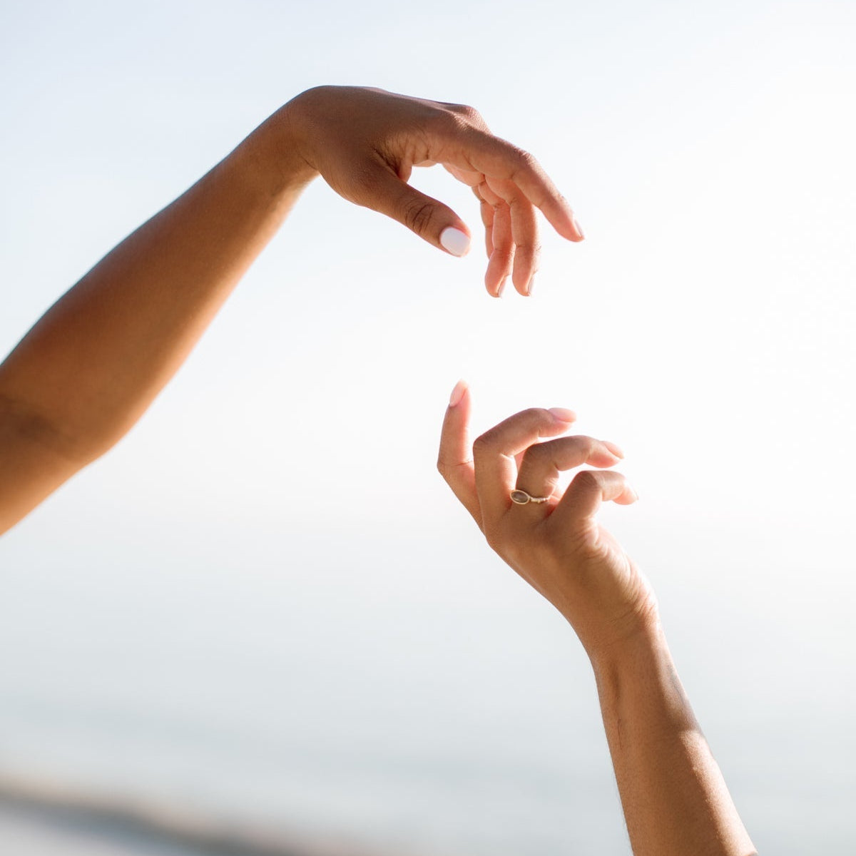 Two hands reaching toward each other against a soft, hazy sky, evoking a calm, dreamlike mood