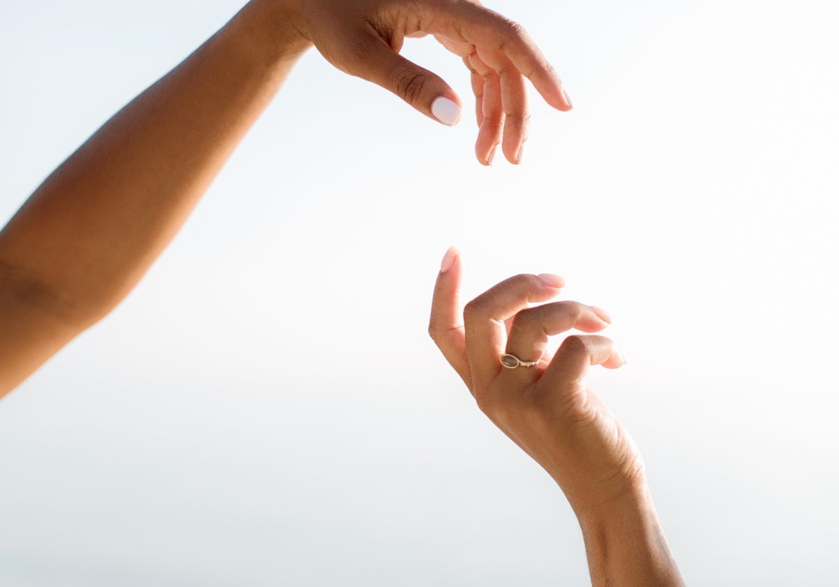 Two hands reaching toward each other against a soft, hazy sky, evoking a calm, dreamlike mood