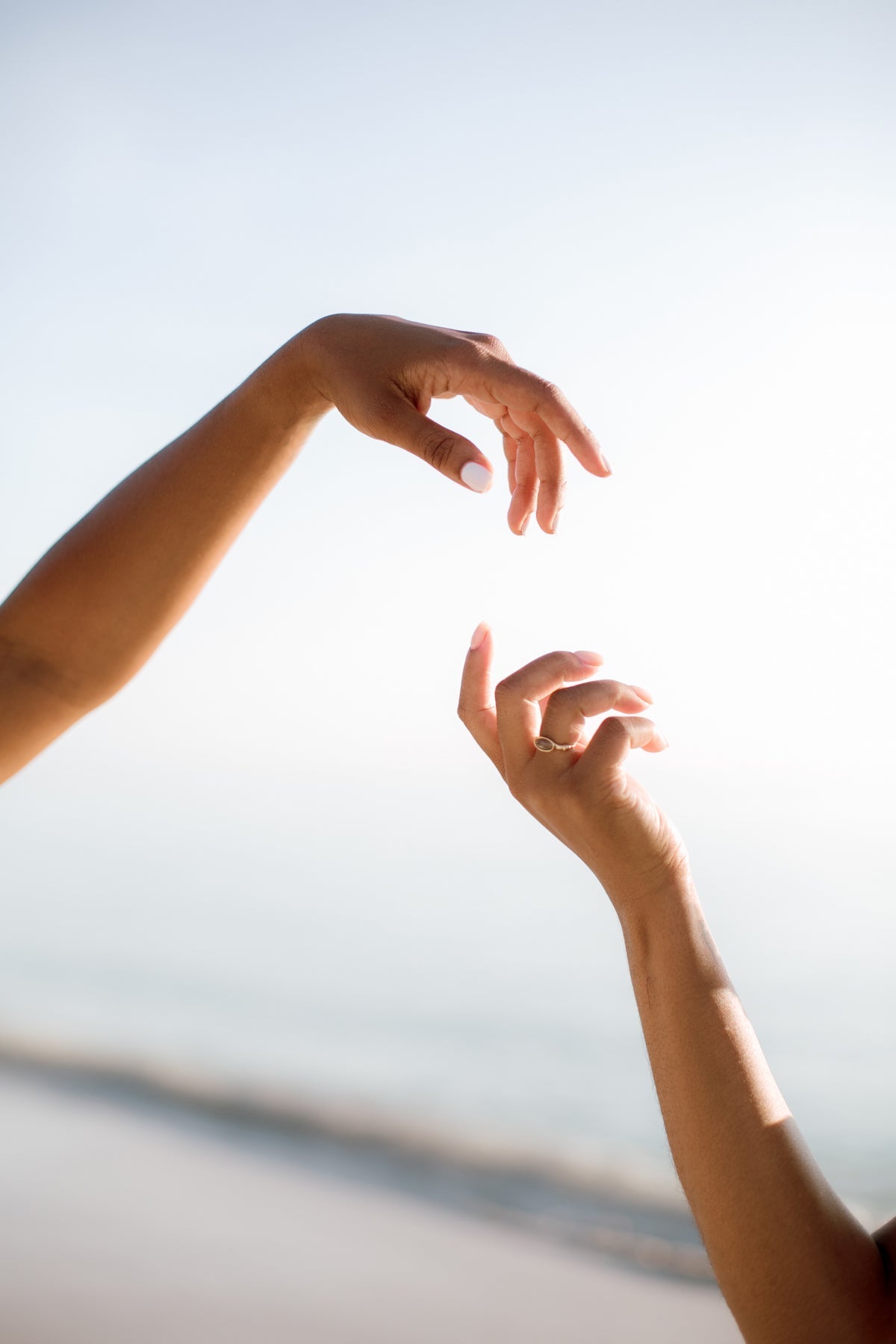 Two hands reaching toward each other against a soft, hazy sky, evoking a calm, dreamlike mood