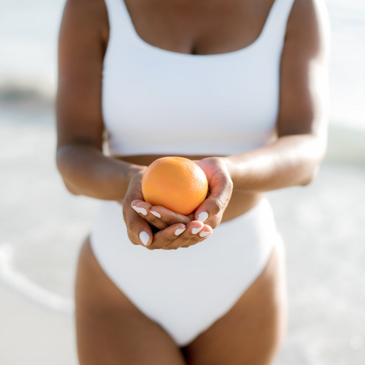 Woman in a white bikini holding an orange at the beach