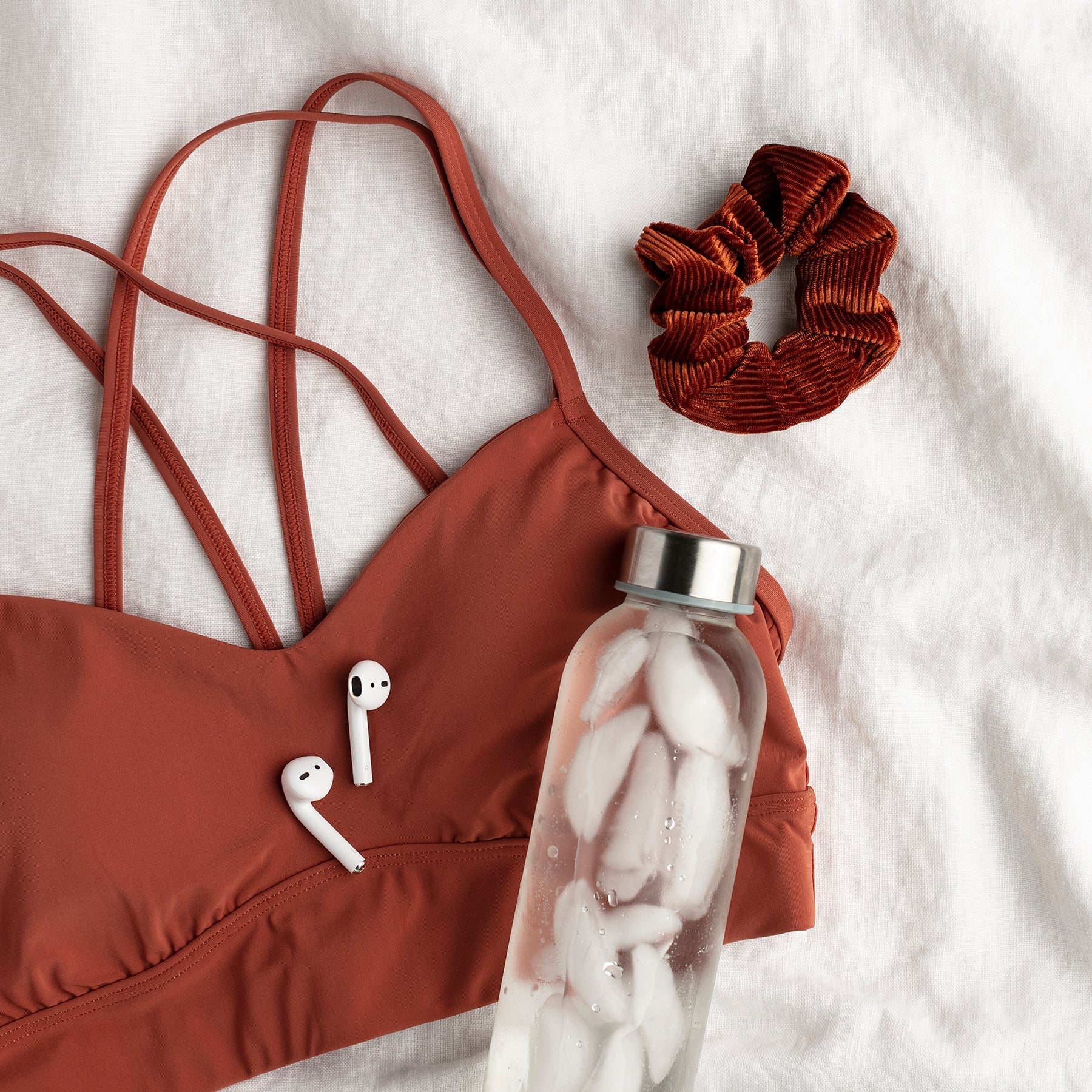 Flat lay of a workout sports bra, scrunchie, wireless earbuds, and water bottle