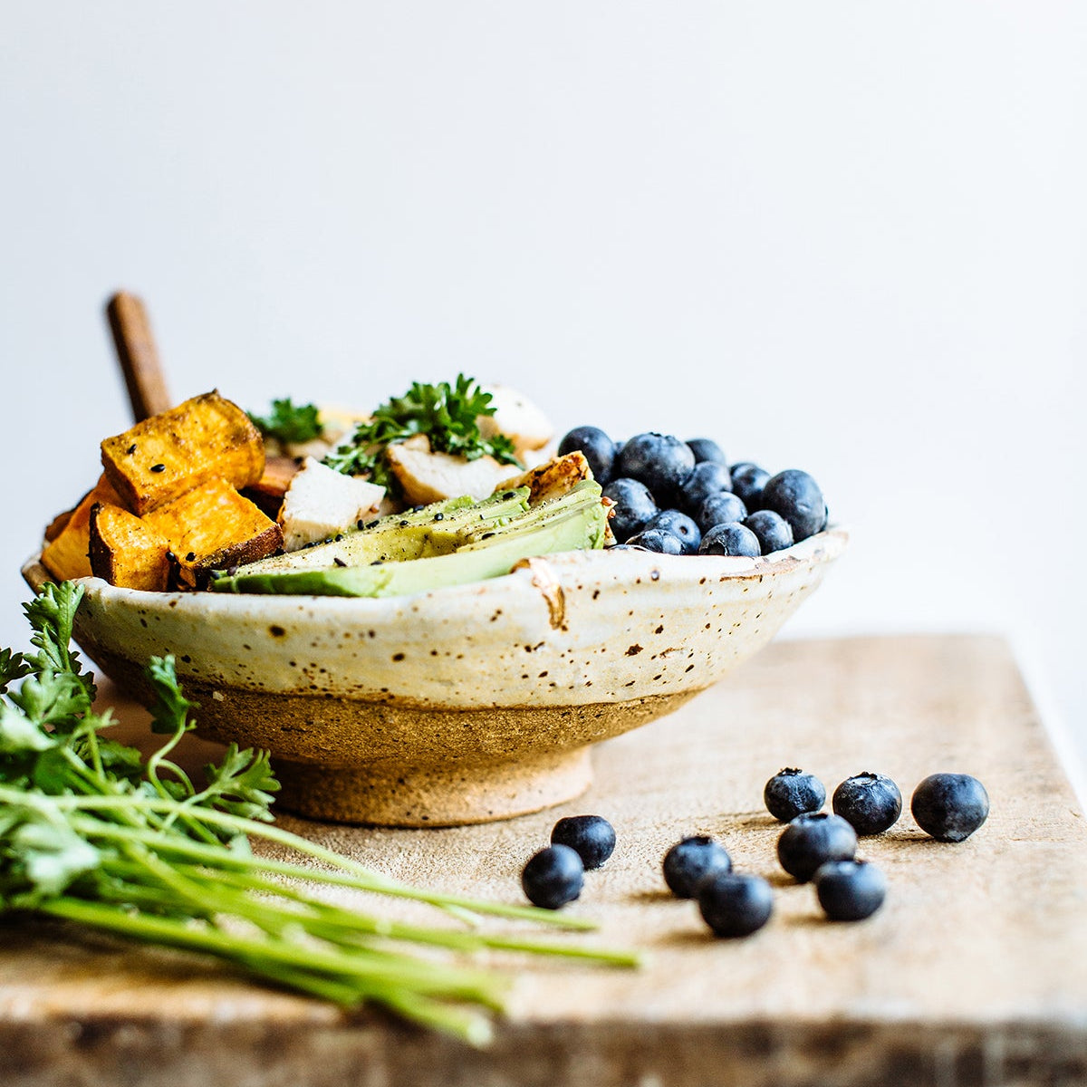 Grain bowl with tofu, greens and blueberries on a wooden board