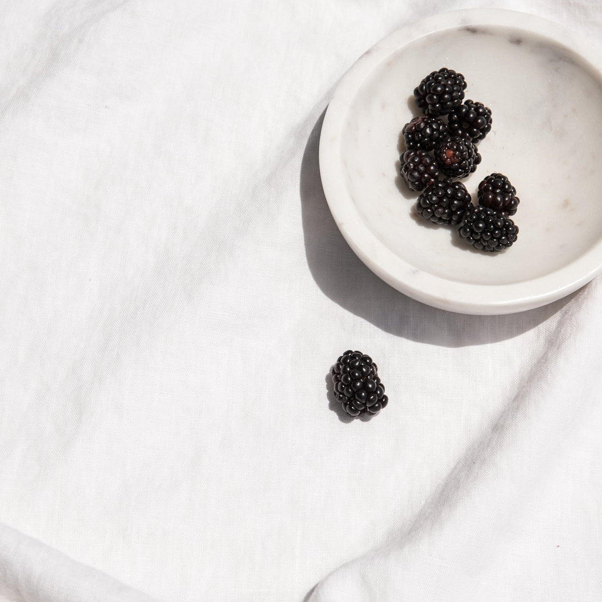 Blackberries in a small white bowl on linen