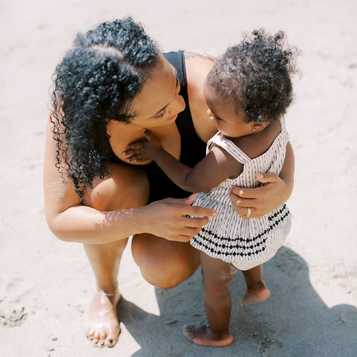 Mother crouching down and smiling at her toddler on a sandy beach