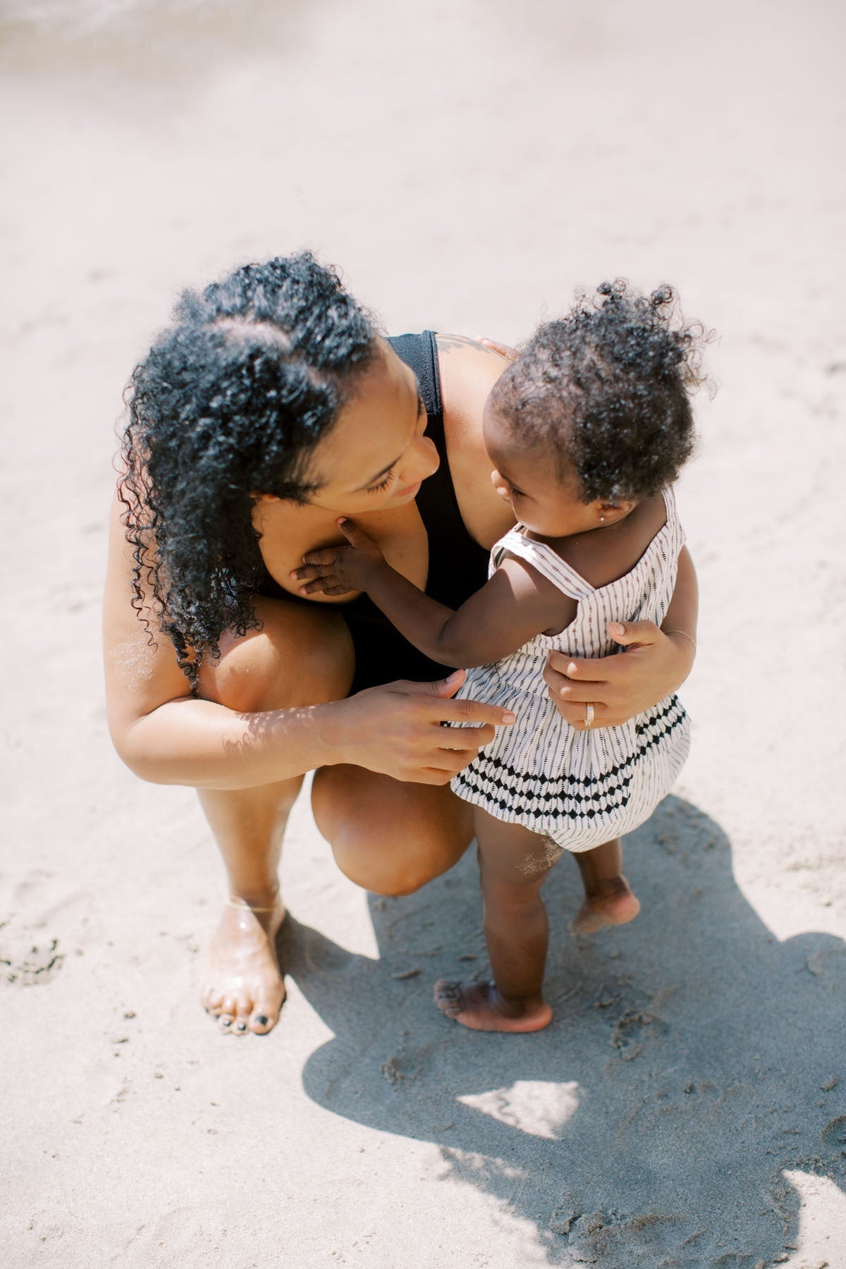 Mother crouching down and smiling at her toddler on a sandy beach