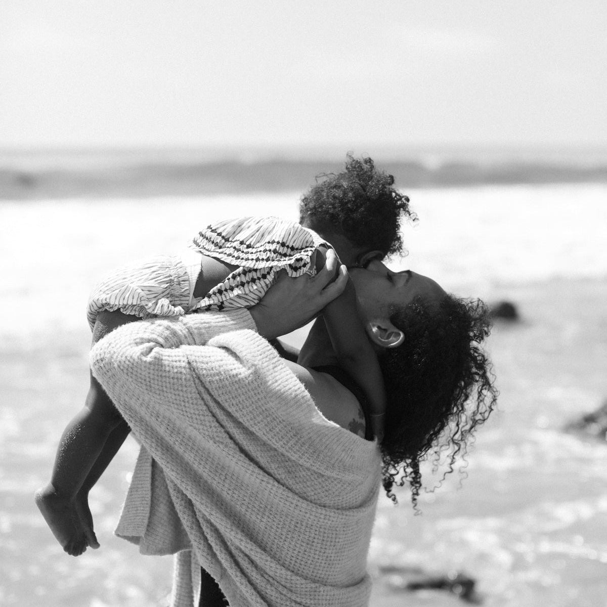 Black-and-white photo of a mother carrying her child on her back at the beach