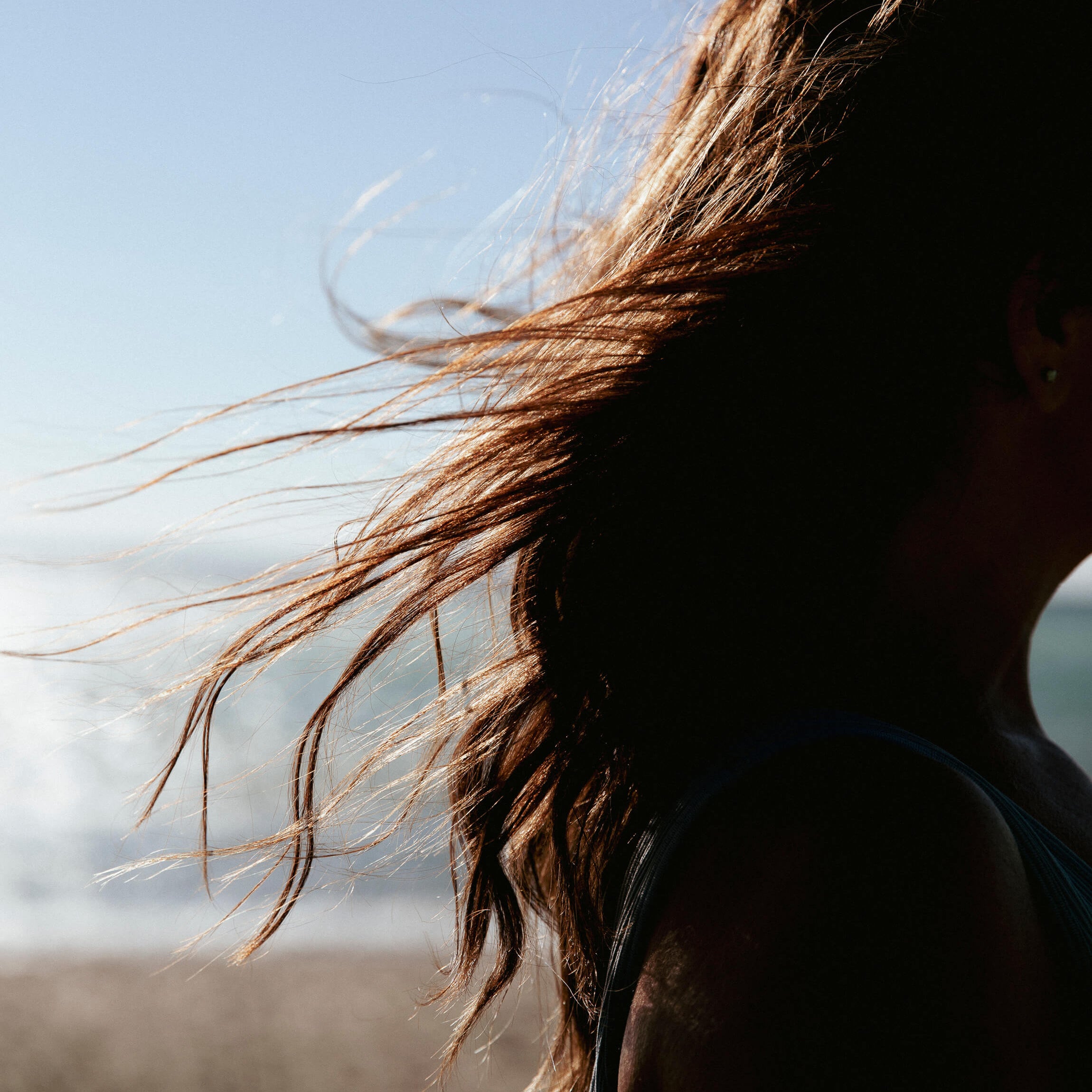 Woman with long, healthy hair blowing in the wind outdoors at golden hour