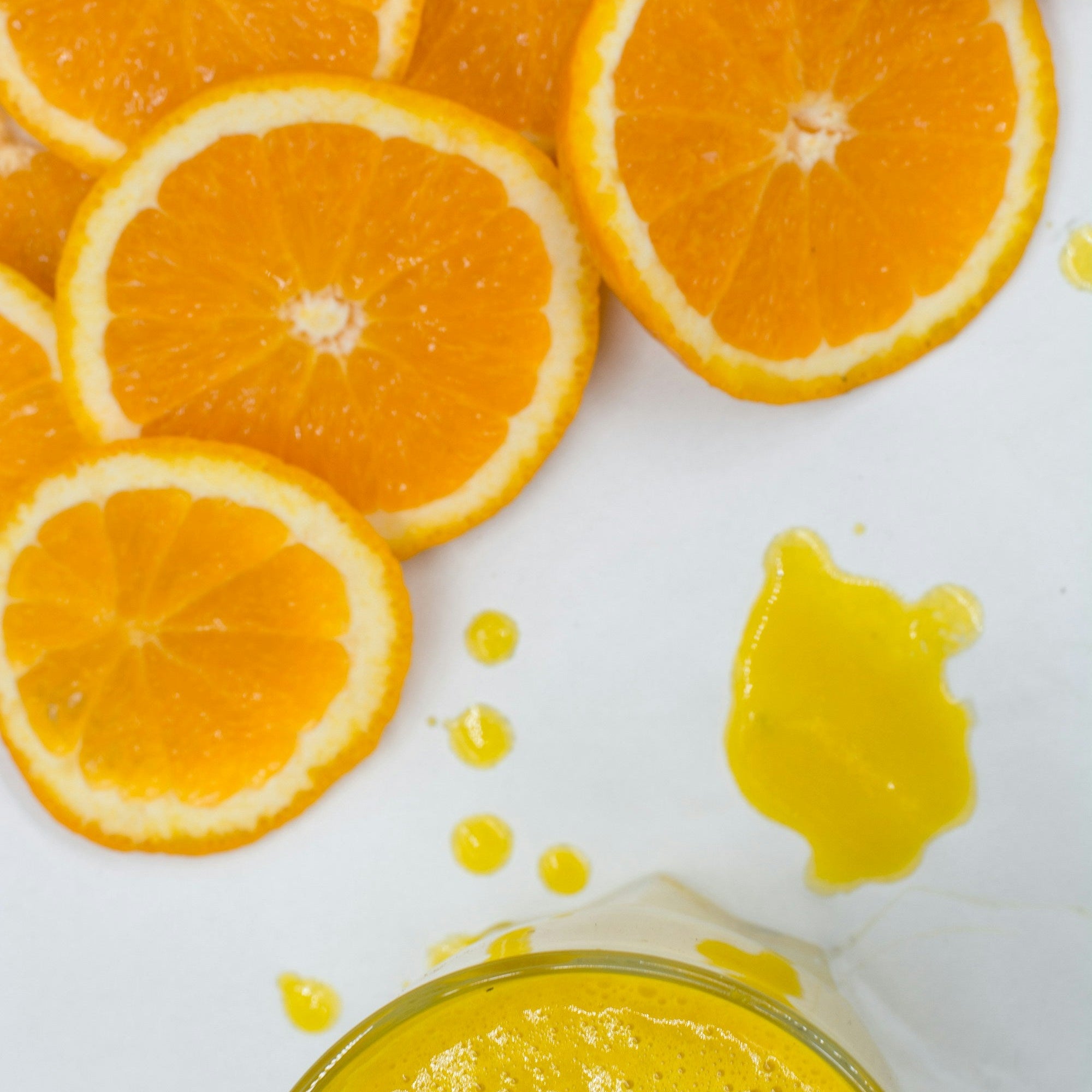 Sliced oranges and a glass of orange juice arranged on a white surface
