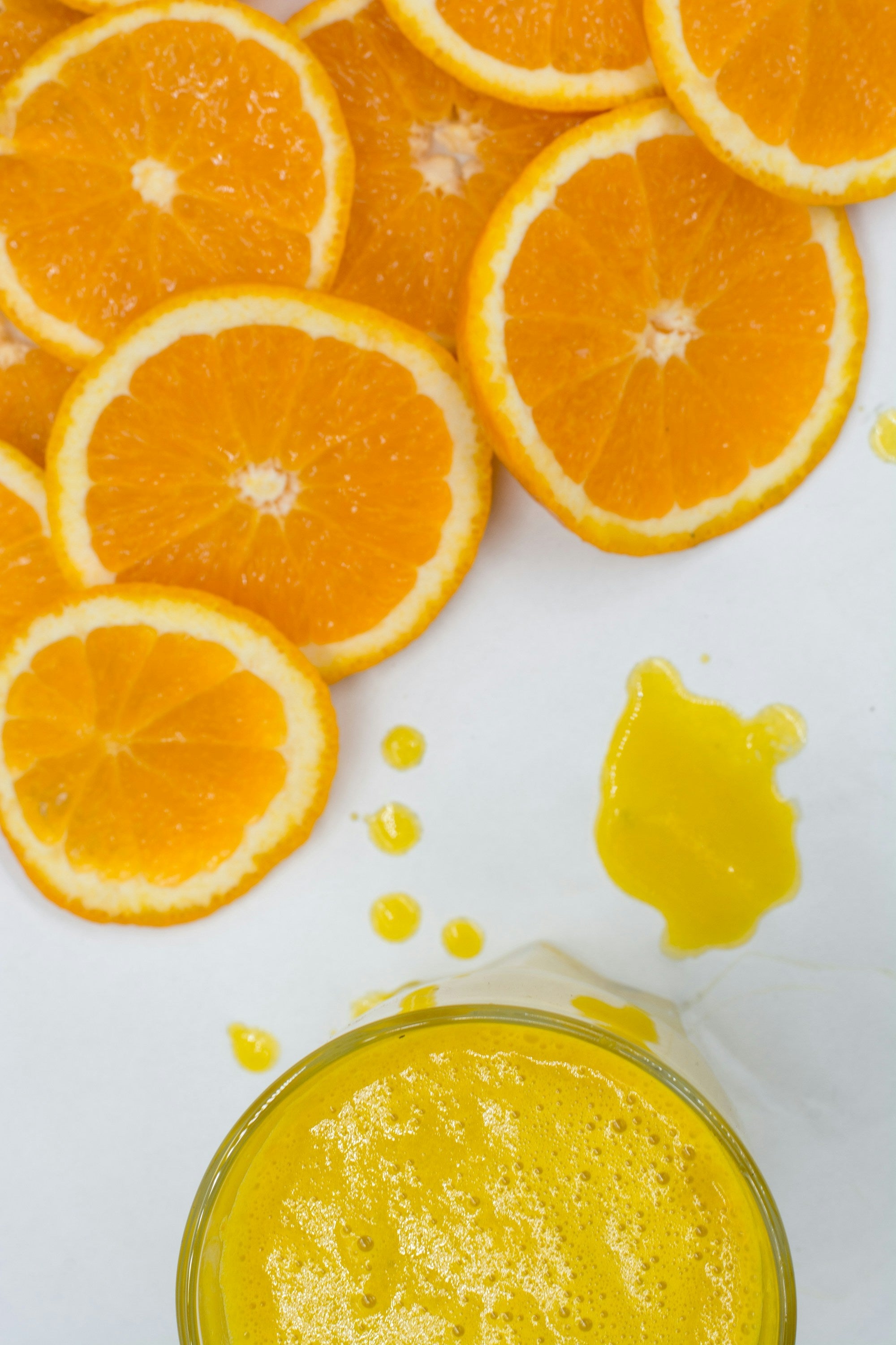 Sliced oranges and a glass of orange juice arranged on a white surface