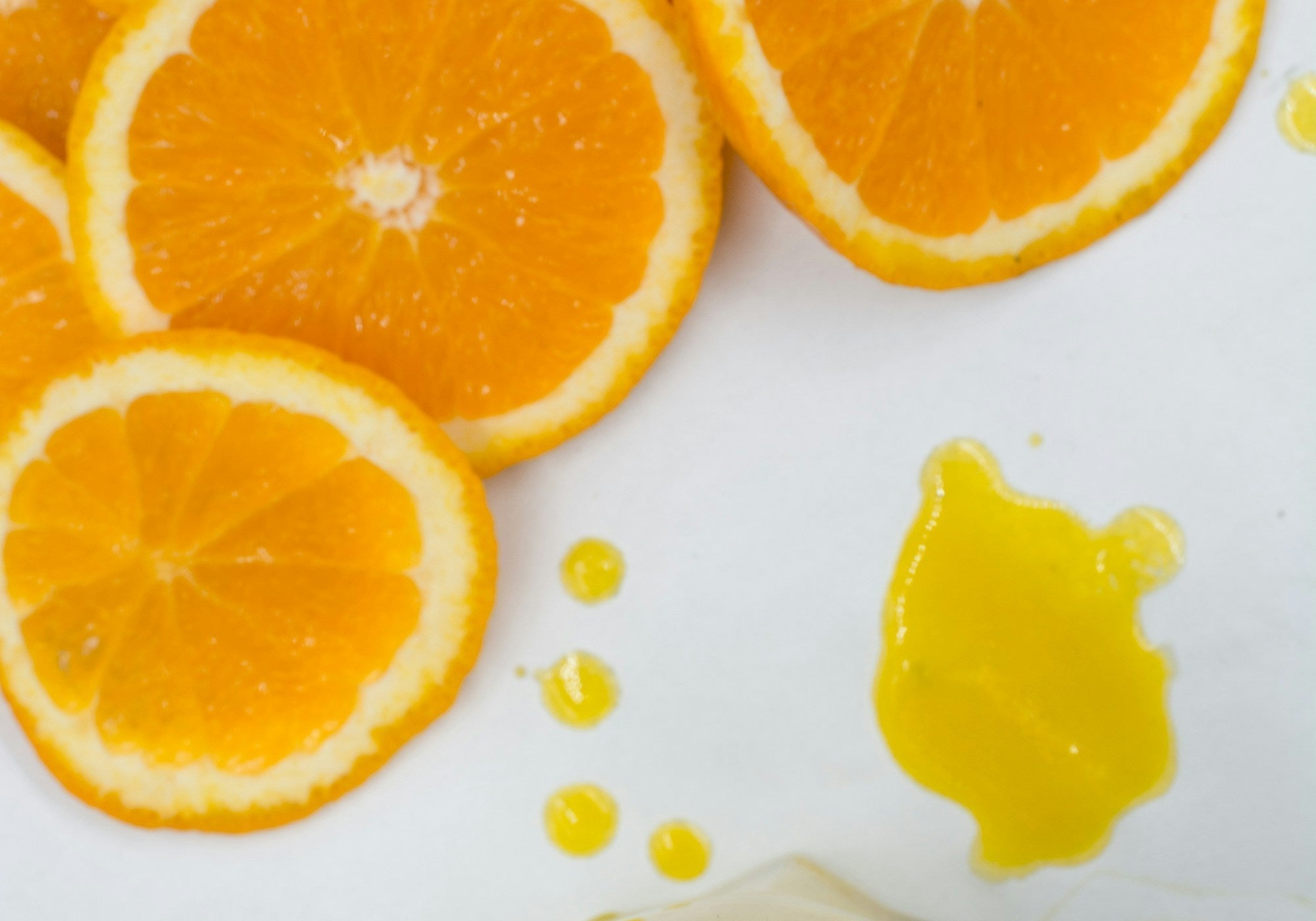 Sliced oranges and a glass of orange juice arranged on a white surface