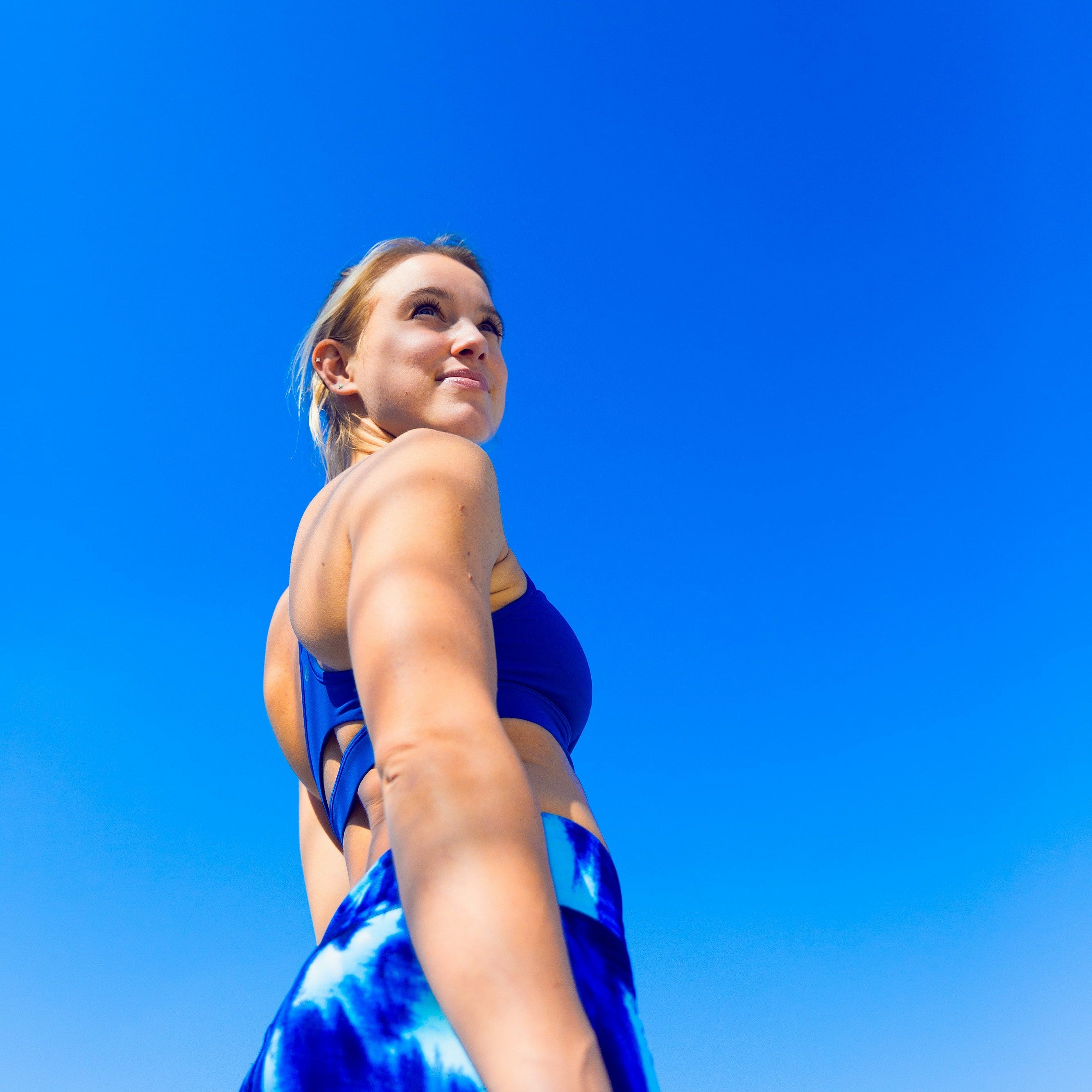 Female swimmer in a blue swimsuit, shot from a low angle against a clear blue sky