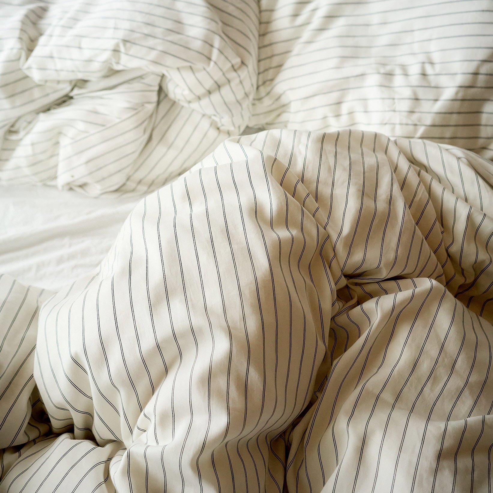 Rumpled striped bed sheets in soft neutral tones, evoking a calm bedtime setting