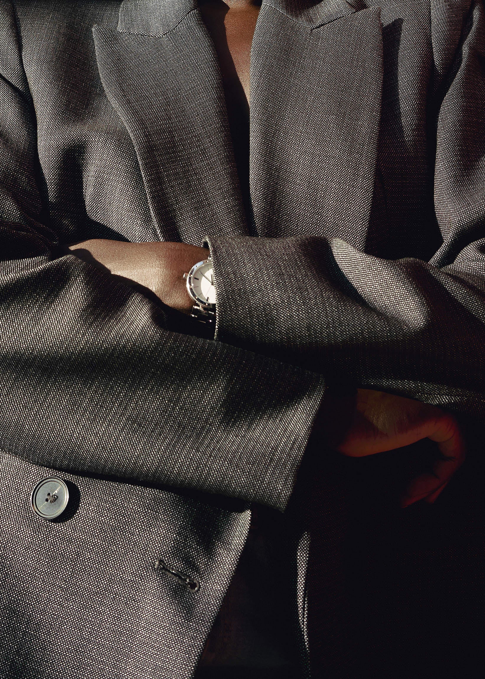 Close-up of a person in a tailored gray blazer with arms crossed, wearing a silver wristwatch