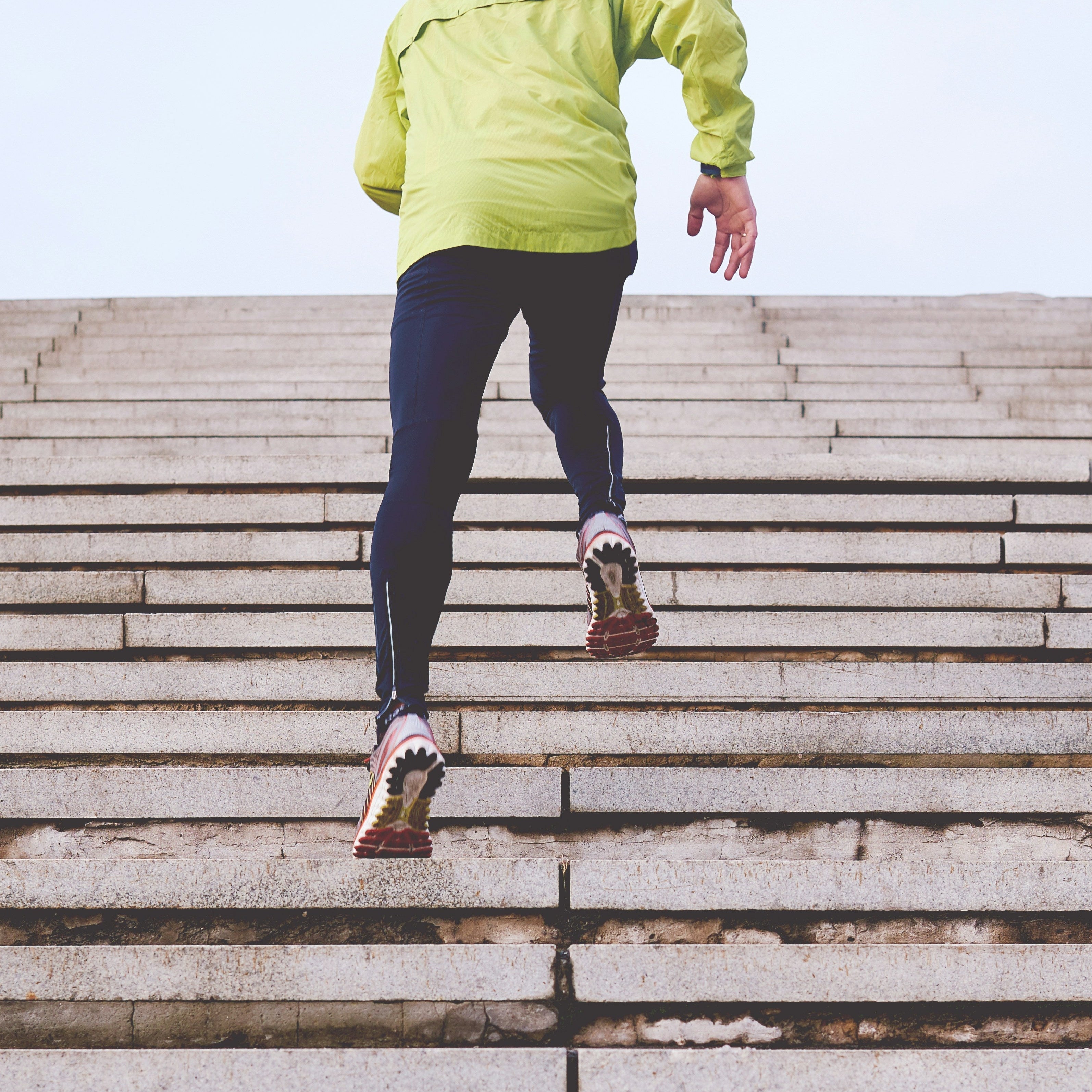Person in a bright yellow jacket energetically running up outdoor stairs