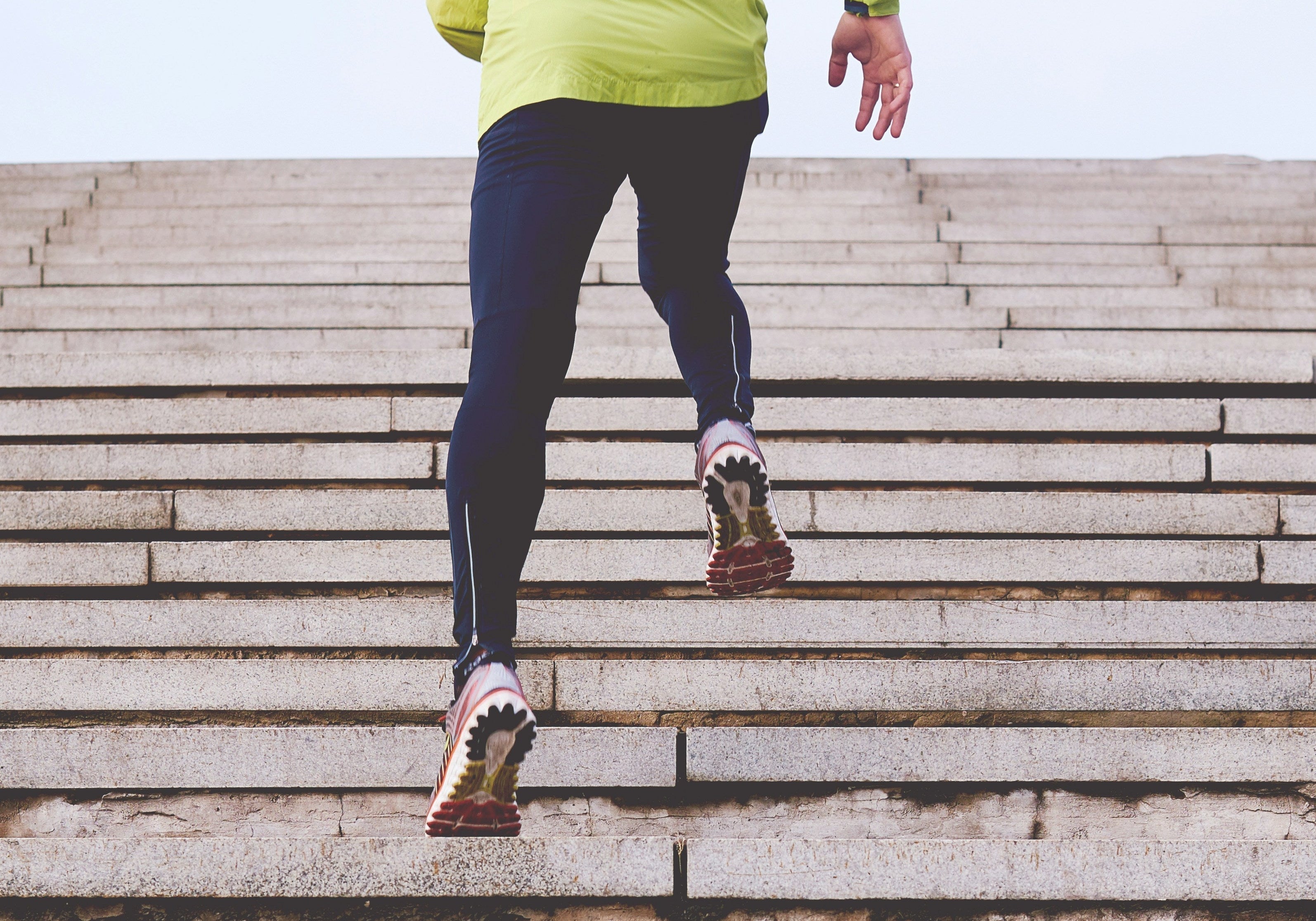 Runner in a bright green jacket climbing outdoor stone steps