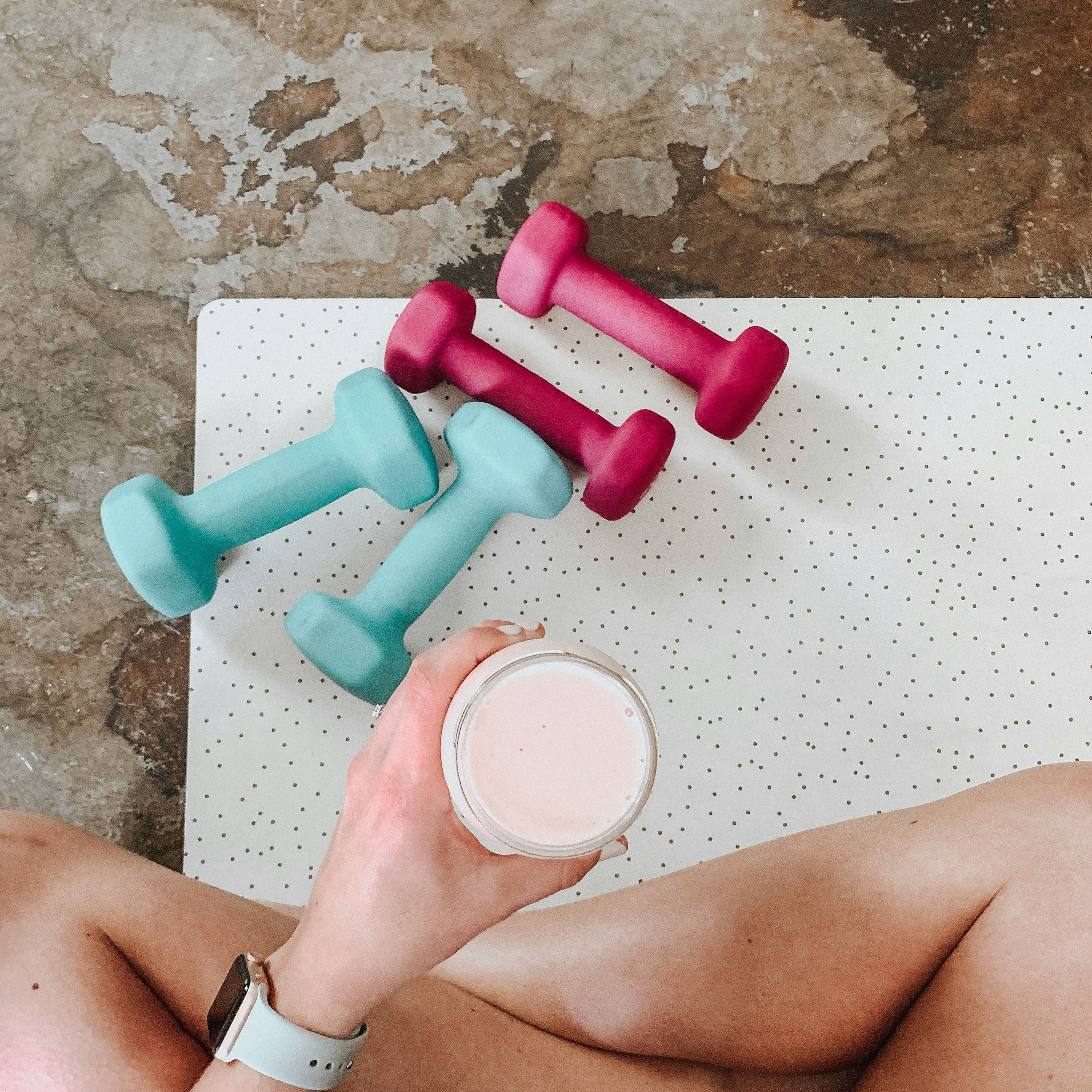 Overhead view of pink and teal dumbbells beside a person holding a smoothie