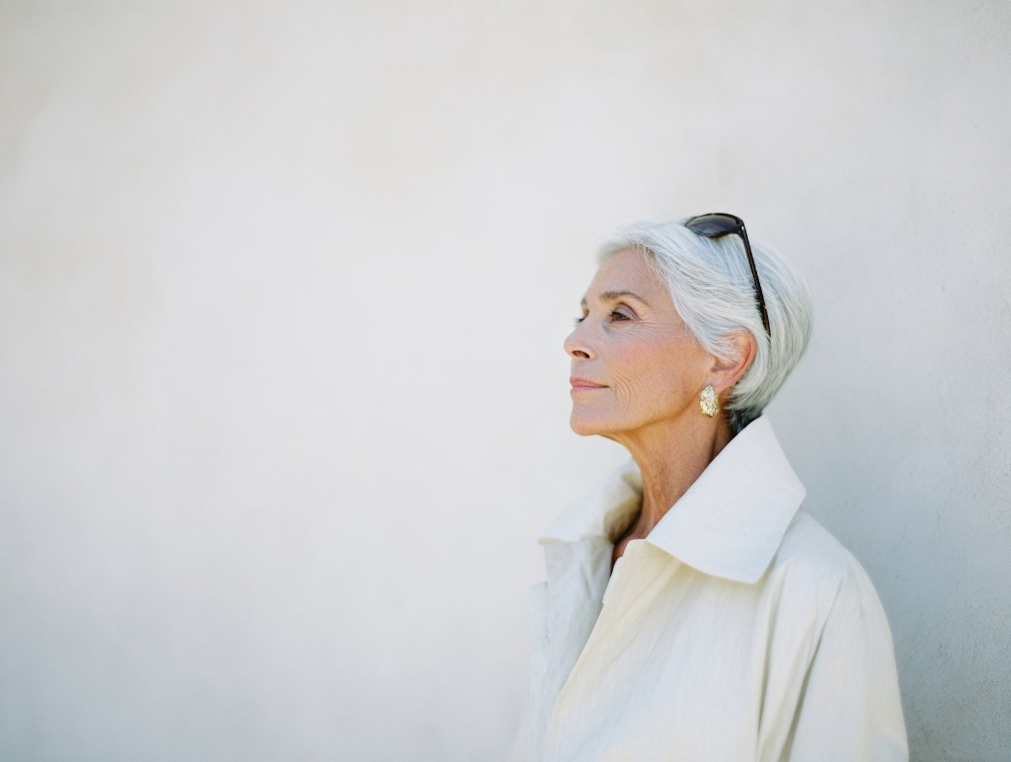 Older woman with silver hair in a white coat looking upward
