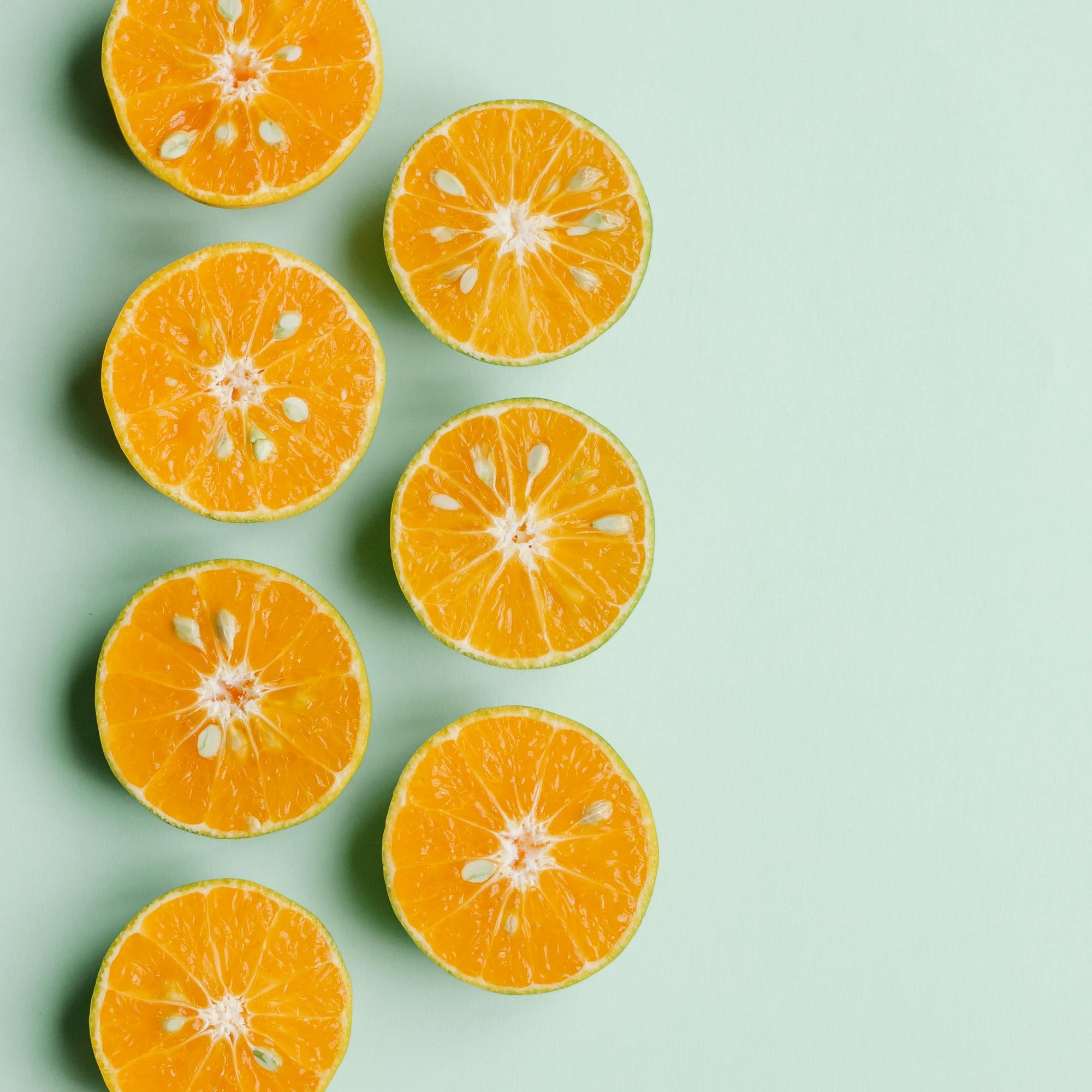 Halved oranges arranged in rows on a pale mint background