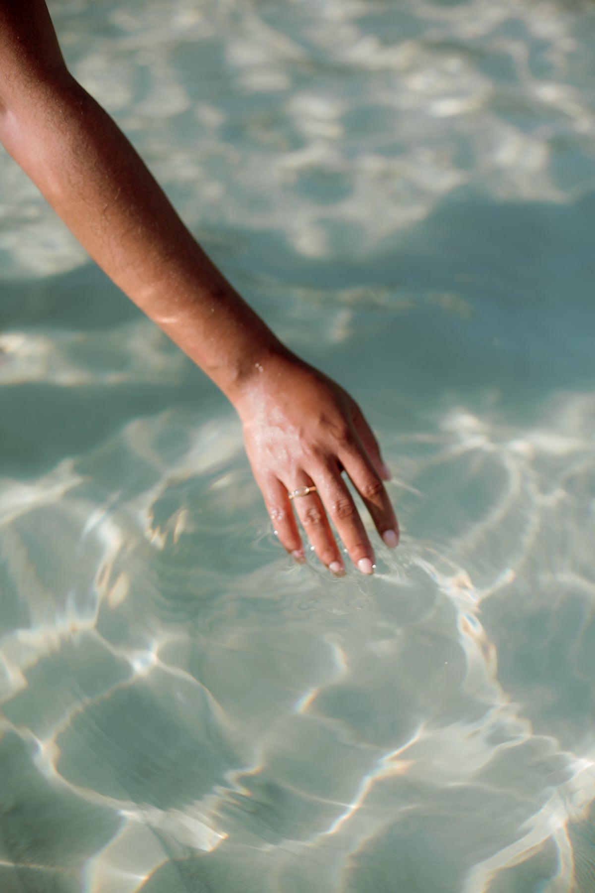 A hand resting in clear, sunlit turquoise water
