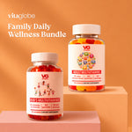 Two Vitaglobe dietary supplement bottles displayed on pink pedestals against a peach background. The front bottle is labeled 'Kid's Multivitamins' and contains red gummies, while the rear bottle is labeled 'Adult Multivitamins' and contains a multicolor mix of gummies.