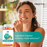 Woman eating a gummy vitamin with a bottle of Vitaglobe Calcium 500 mg gummies in front of her.