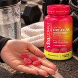 VitaPower by Vita Globe Sugar-Free Creatine Monohydrate Gummies, Watermelon, with a hand holding pink gummies beside a water bottle and gym gear