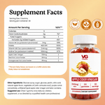 A supplement facts label and a bottle of VG Vitality Apple Cider Vinegar gummies on a peach background. The label includes serving size, calories, carbohydrates, sugars, vitamins, and other ingredients, with icons indicating 100% natural, non-GMO, and gluten-free.