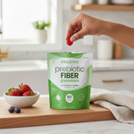 Vitaglobe prebiotic fiber gummies packaging with a hand holding a gummy and a bowl of strawberries on a kitchen counter.
